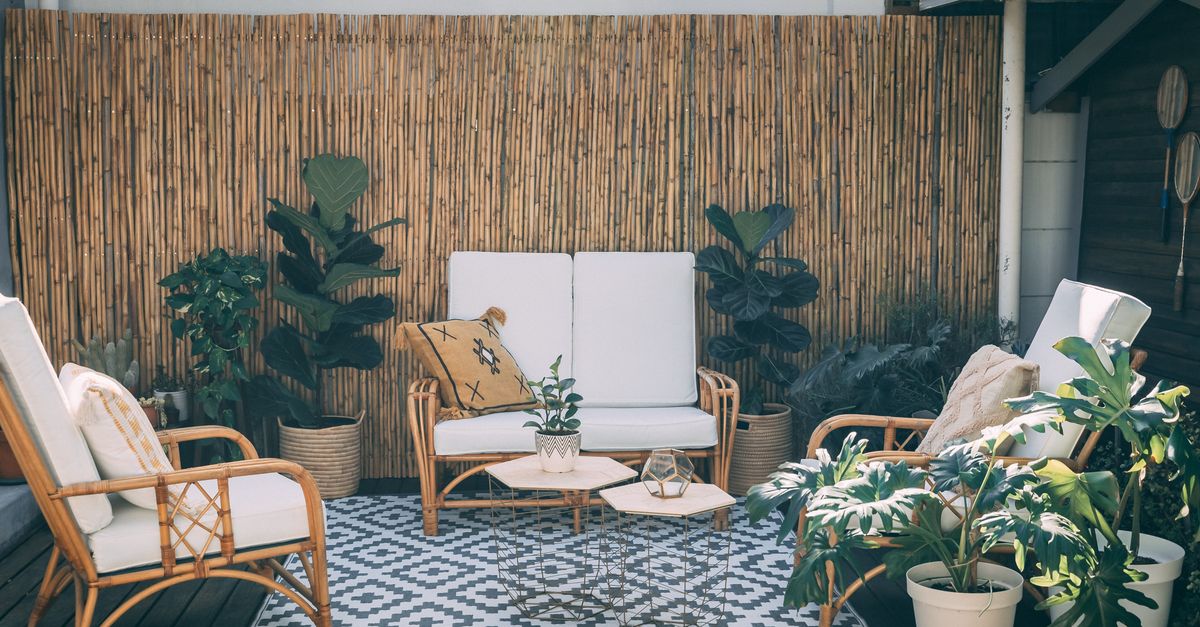 Coin balcon cosy avec fauteuils en rotin coussins blancs, tapis à motifs géométriques, plantes vertes et claustra en bambou en fond.