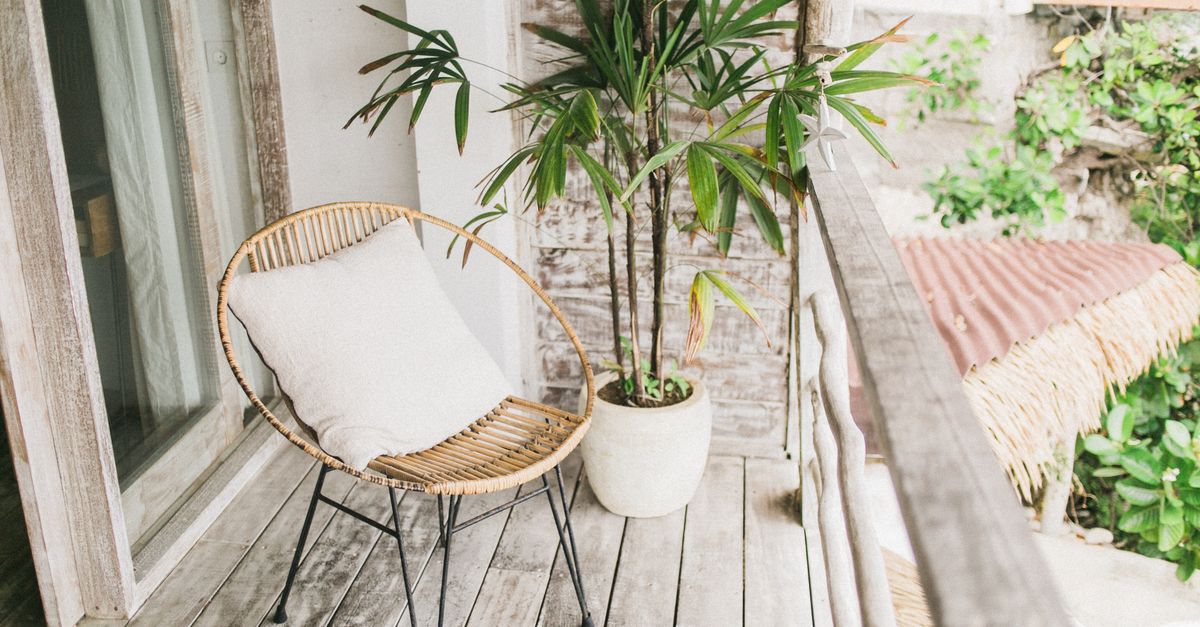 Un fauteuil en rotin avec un coussin blanc posé sur une terrasse en bois à côté d'une plante verte en pot.