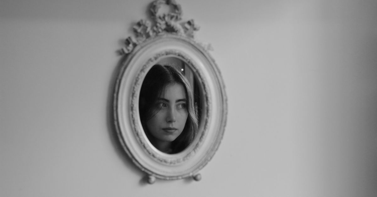 Miroir ovale à cadre blanc orné, accroché au mur, reflétant le visage d'une femme en noir et blanc.