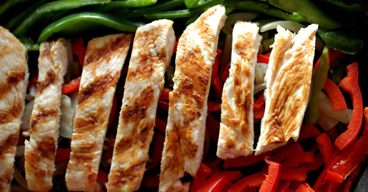 Lanières de poulet grillé disposées sur un lit de poivrons rouges et d'oignons émincés dans une poêle.
