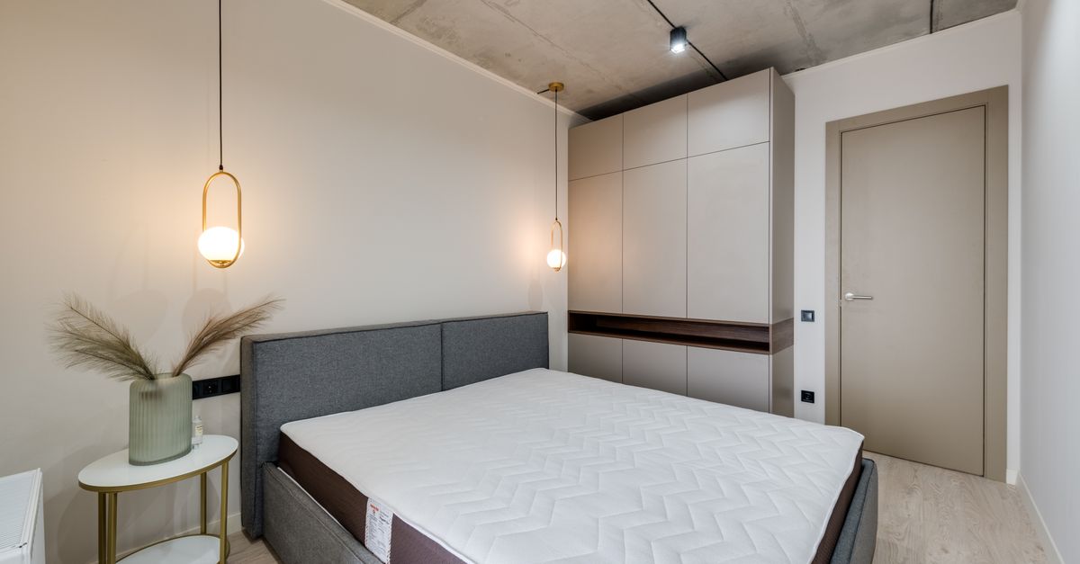 Chambre moderne avec deux suspensions lumineuses dorées suspendues au plafond en béton de part et d'autre d'un lit gris.