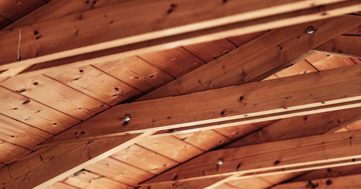 Gros plan sur des poutres en bois apparentes d'un plafond avec des boulons métalliques visibles.