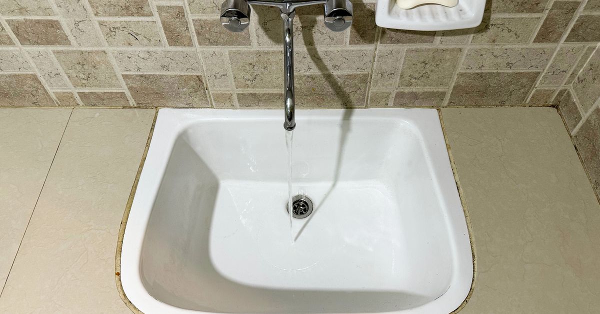 Évier blanc en céramique vu de dessus avec un filet d'eau coulant du robinet vers la bonde de vidange.