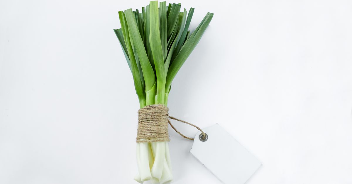 Un bouquet de poireaux entiers, feuilles vertes et base blanche, attaché avec de la ficelle sur fond blanc, avec une étiquette vierge accrochée.