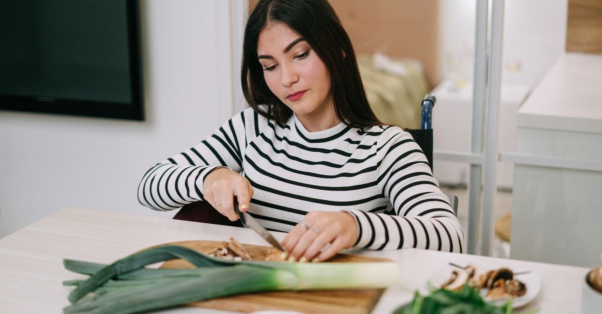 Une femme en pull rayé découpe un poireau frais sur une planche en bois dans sa cuisine.
