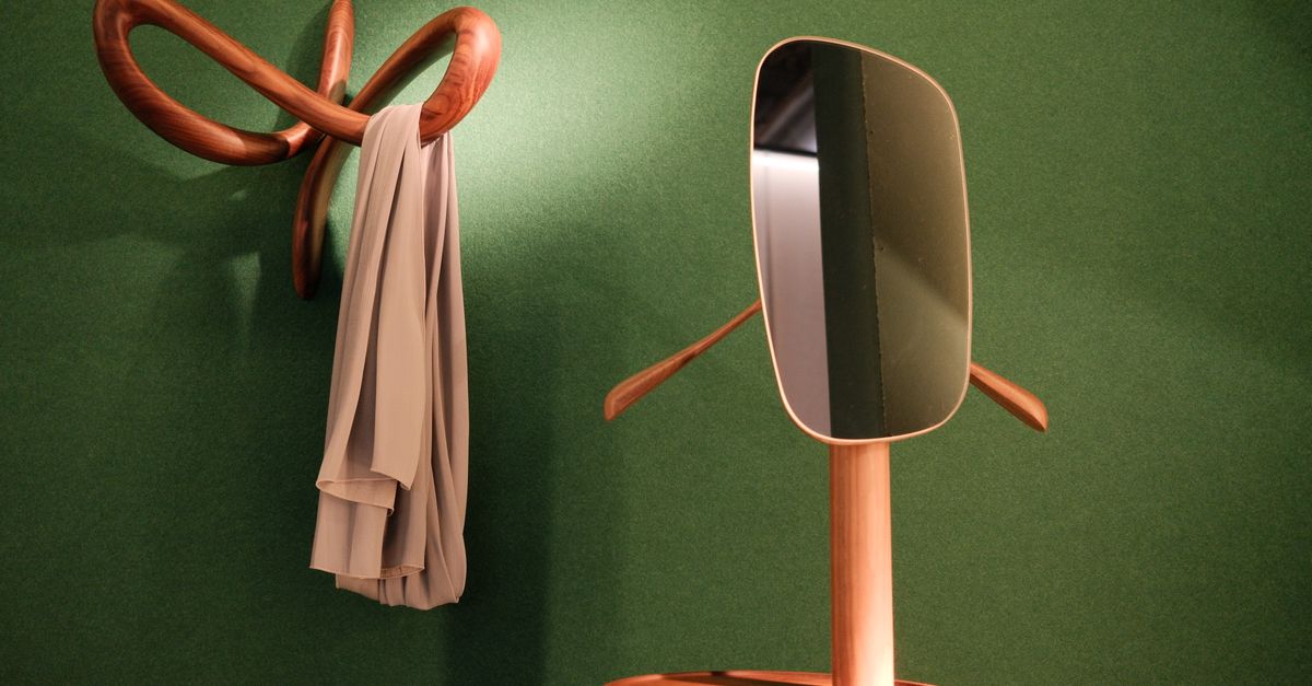 Dans une entrée aux murs verts, un portemanteau en bois sculpté retient une écharpe et un valet de nuit équipé d'un miroir se tient à côté.