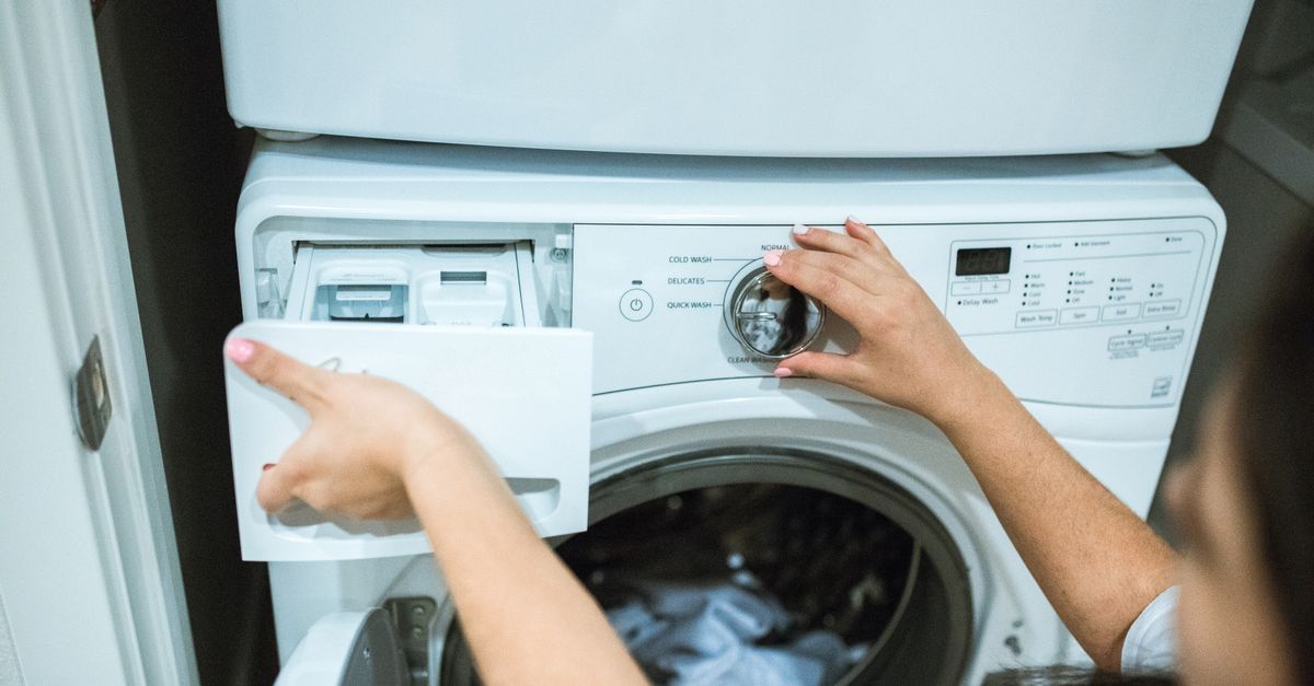 Une personne ouvre le tiroir à détergent d'un lave-linge et appuie sur les boutons du tableau de commande.