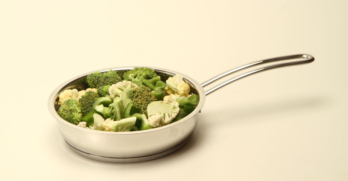 Un sauté de fleurettes de brocoli et de chou-fleur vert et blanc dans une poêle en acier inoxydable sur fond clair.