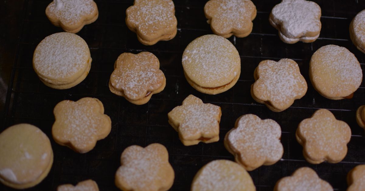 Des biscuits sablés en forme de fleurs et de ronds, saupoudrés de sucre glace, disposés sur une grille de refroidissement.