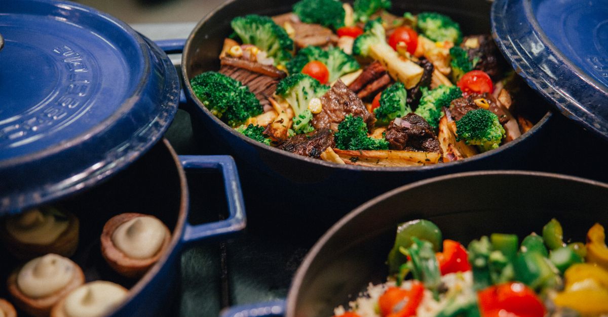 Des bouquets de brocolis sautés avec des morceaux de viande et des tomates cerises dans une cocotte en fonte bleue.