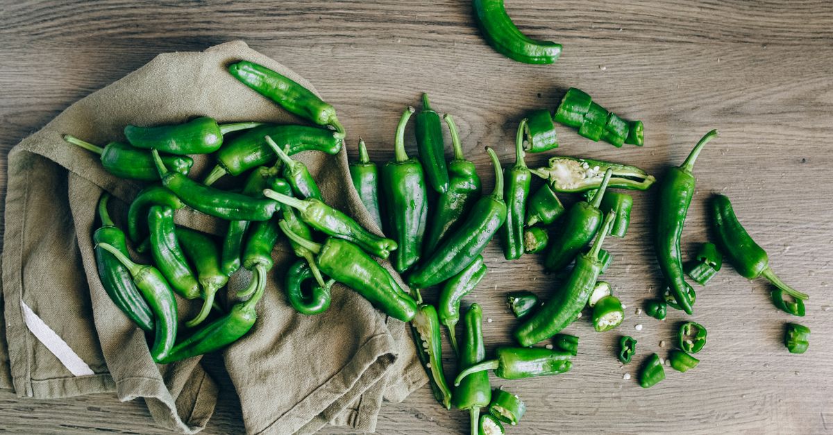 Des piments verts entiers éparpillés sur une planche en bois avec un linge en toile.