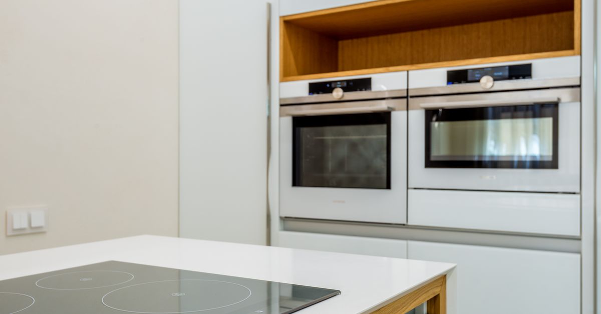Un plan de travail compact équipé d'une plaque à induction, avec deux fours encastrés en arrière-plan dans une kitchenette moderne.