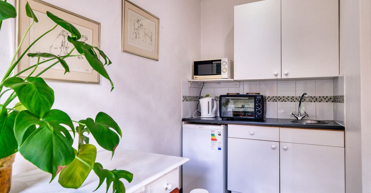Une petite kitchenette compacte avec un four micro-ondes posé sur une étagère au-dessus d'un réfrigérateur et d'une bouilloire électrique.