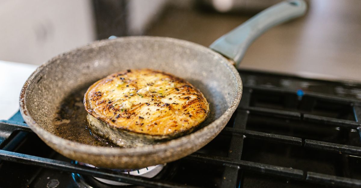 Une tranche ronde et dorée, probablement de polenta, en train de rissoler dans une poêle sur une cuisinière à gaz.