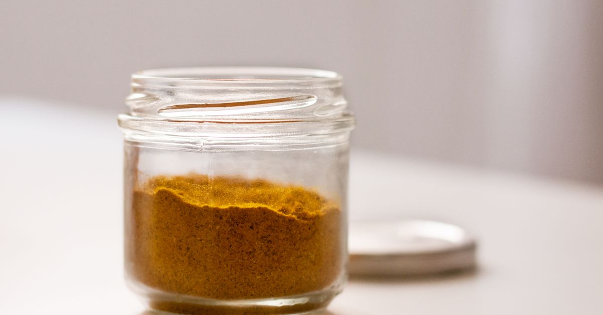 Un pot en verre ouvert contenant une préparation en poudre jaune-orangé, posé sur un plan de travail clair.