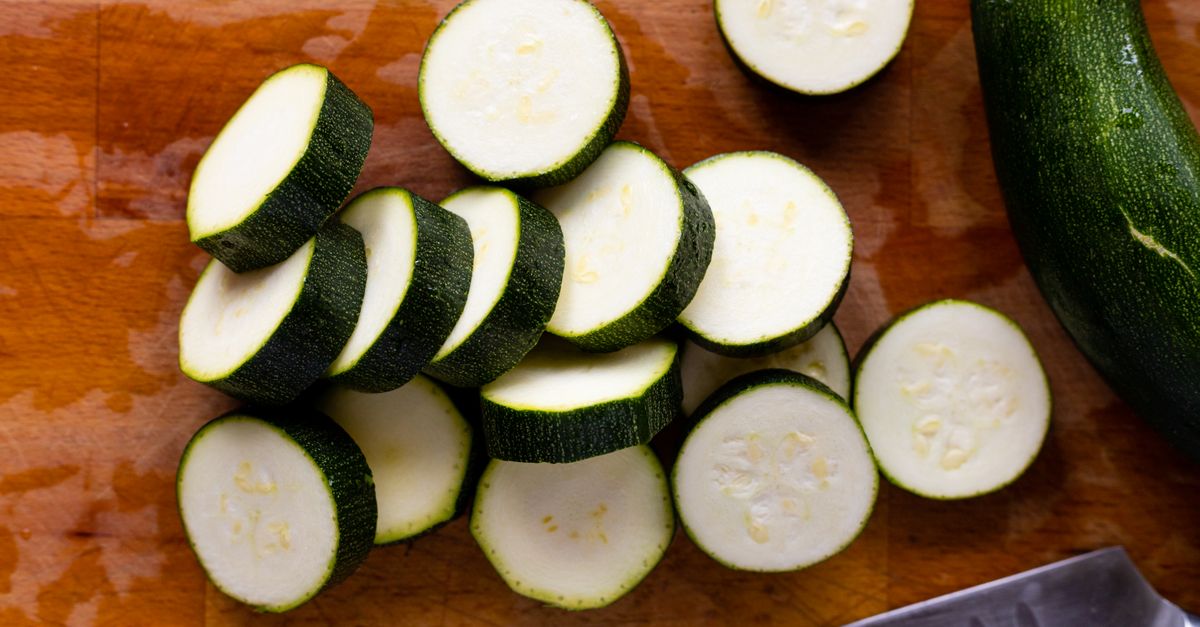 Des rondelles de courgette fraîchement coupées, vues du dessus, disposées sur une planche à découper en bois.