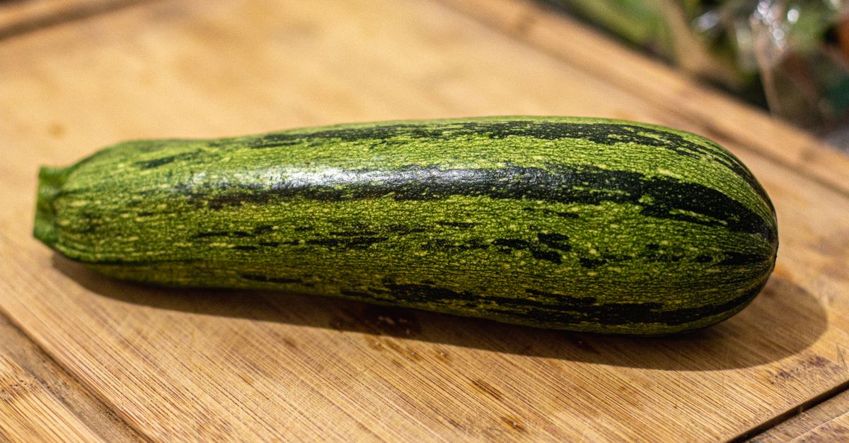 Une courgette entière posée sur une planche en bois.