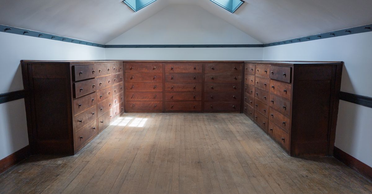 Grenier aménagé avec de grandes commodes en bois intégrées sous les combles et des fenêtres de toit.