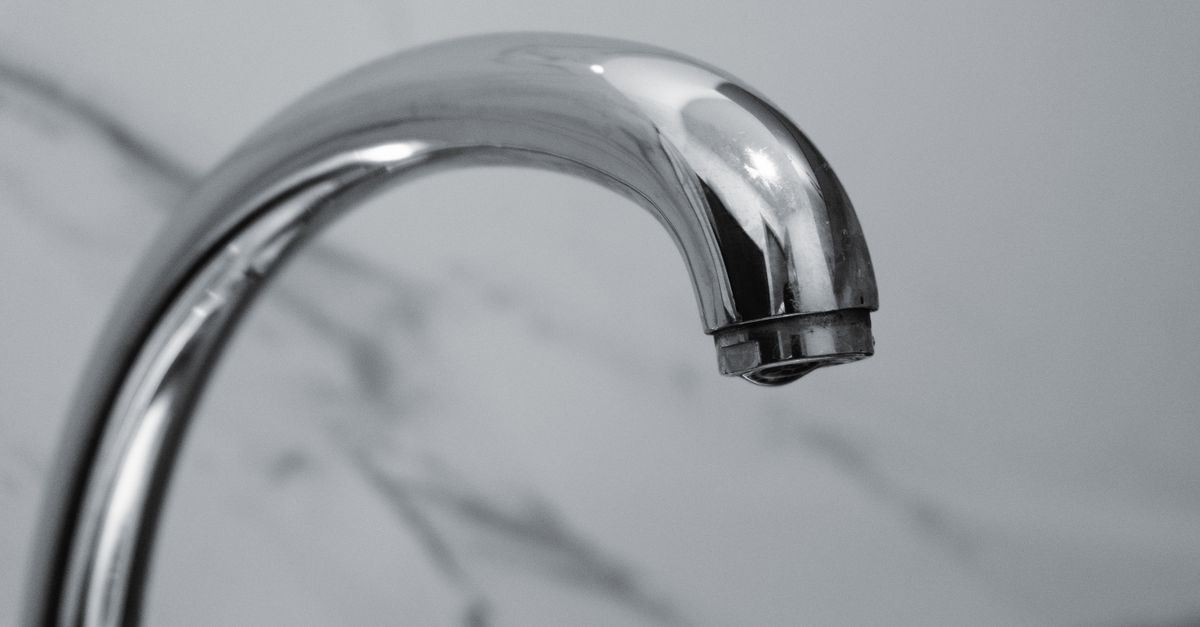 Gros plan sur un robinet chromé brillant avec son bec recourbé, sans trace visible de calcaire, devant un fond en marbre.