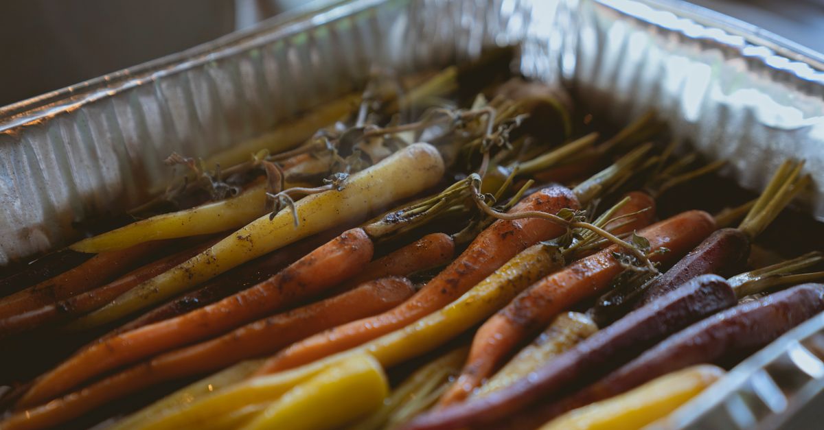 Des carottes entières multicolores avec leurs fanes cuisent dans un plat en aluminium.