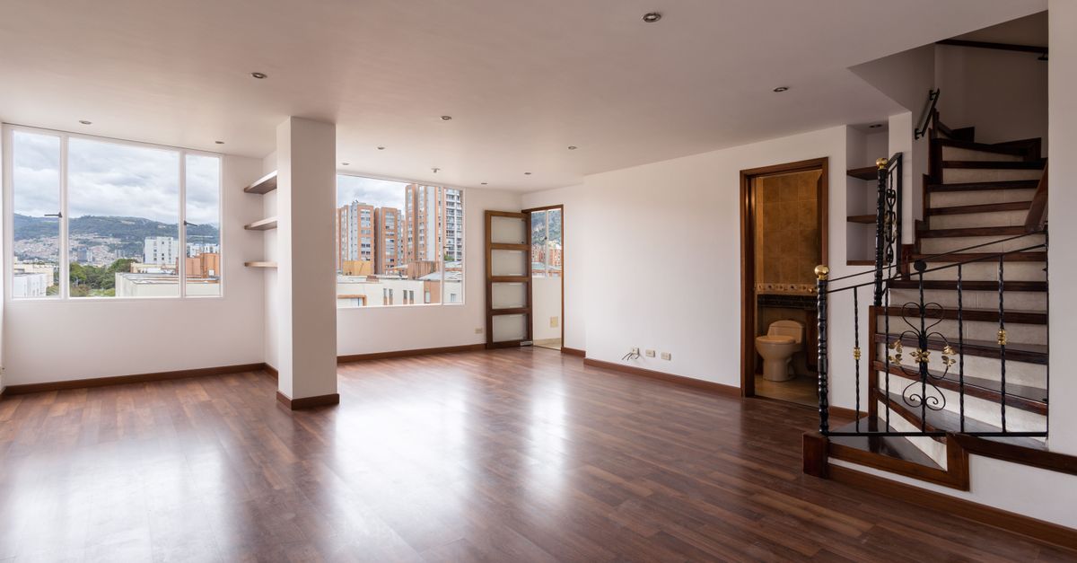 Salon vide avec parquet et escalier en bois visible à droite, avant tout aménagement du recoin sous les marches.