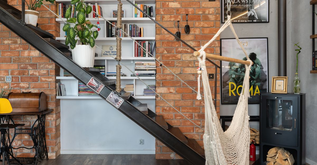 Un escalier métallique habillé d'étagères en bois installées contre un mur de briques dans un angle sous les marches, utilisées pour ranger livres et objets décoratifs.