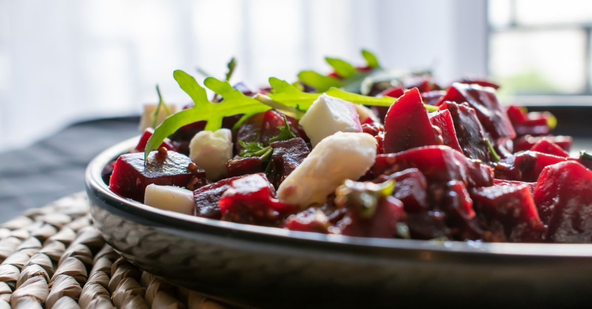Un bol de salade de betteraves cuites coupées en dés avec des morceaux de fromage et de la roquette.