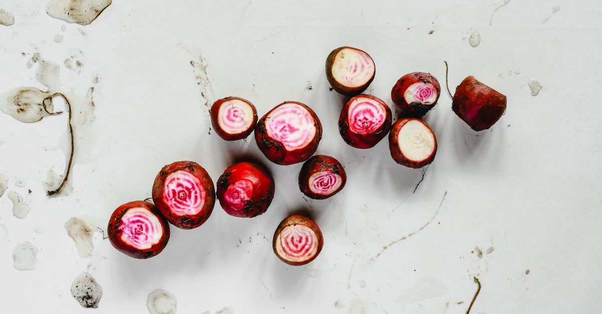 Plusieurs betteraves chioggia coupées en deux, révélant leur chair rose et blanche zébrée, posées sur une surface claire.