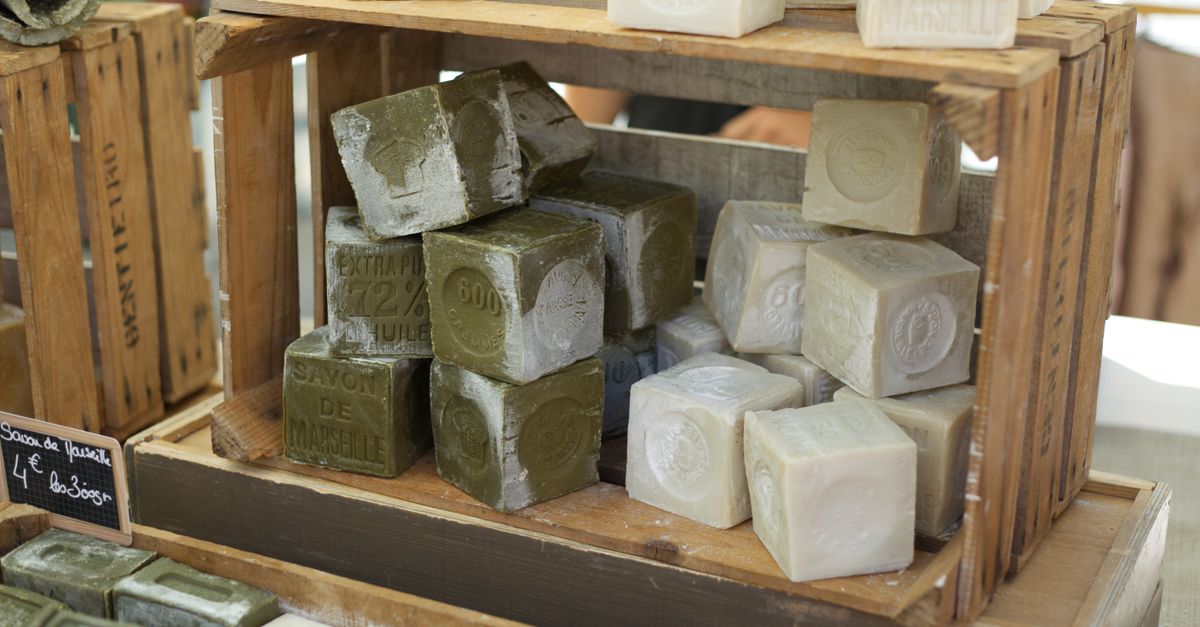 Des cubes de savon de Marseille empilés dans une caisse en bois sur un étal de marché.