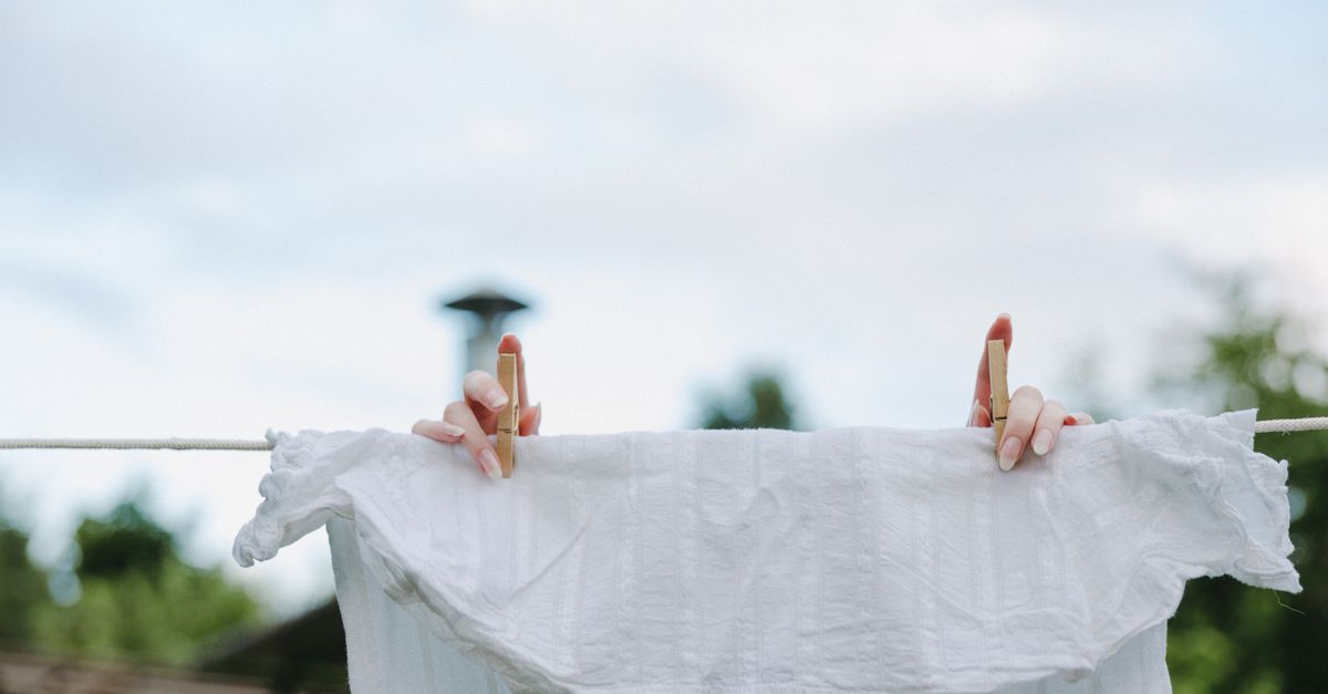 Un linge blanc suspendu à une corde à linge en extérieur, fixé par deux pinces en bois, avec un ciel clair en arrière-plan.
