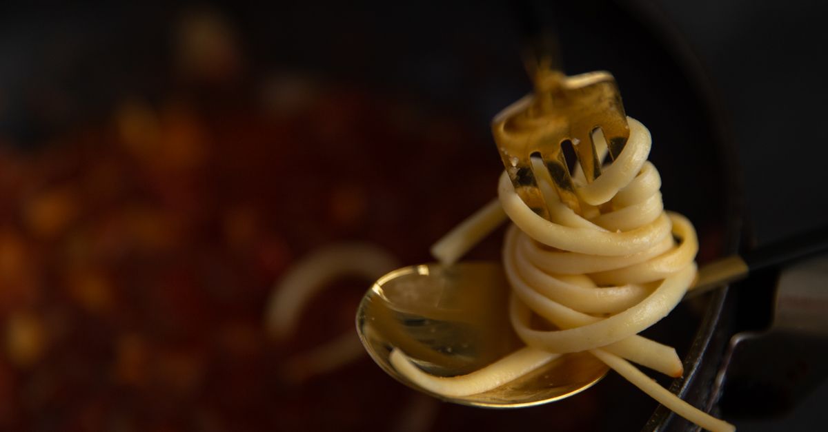 Une fourchette dorée enroule des spaghettis au-dessus d'une sauce bolognaise qui mijote dans une poêle sombre.
