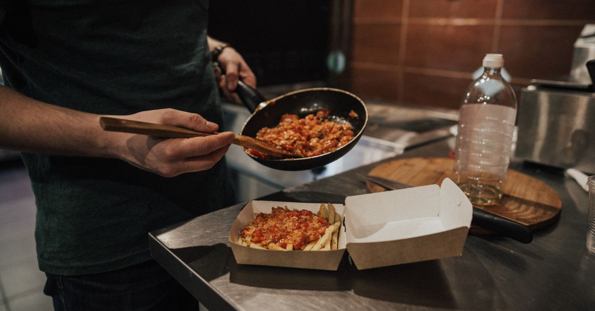 Une personne verse de la sauce tomate depuis une poêle dans une boîte en carton, avec une autre portion déjà servie à côté sur un plan de travail.