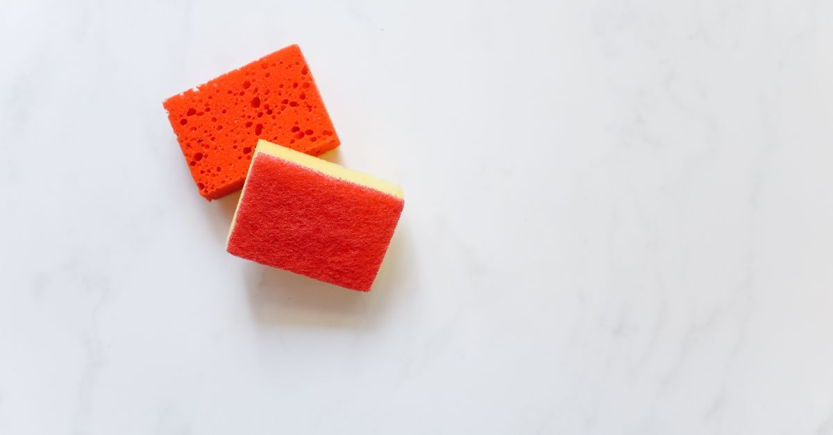 Deux éponges de nettoyage orange et rouge posées sur un plan de travail en marbre blanc.