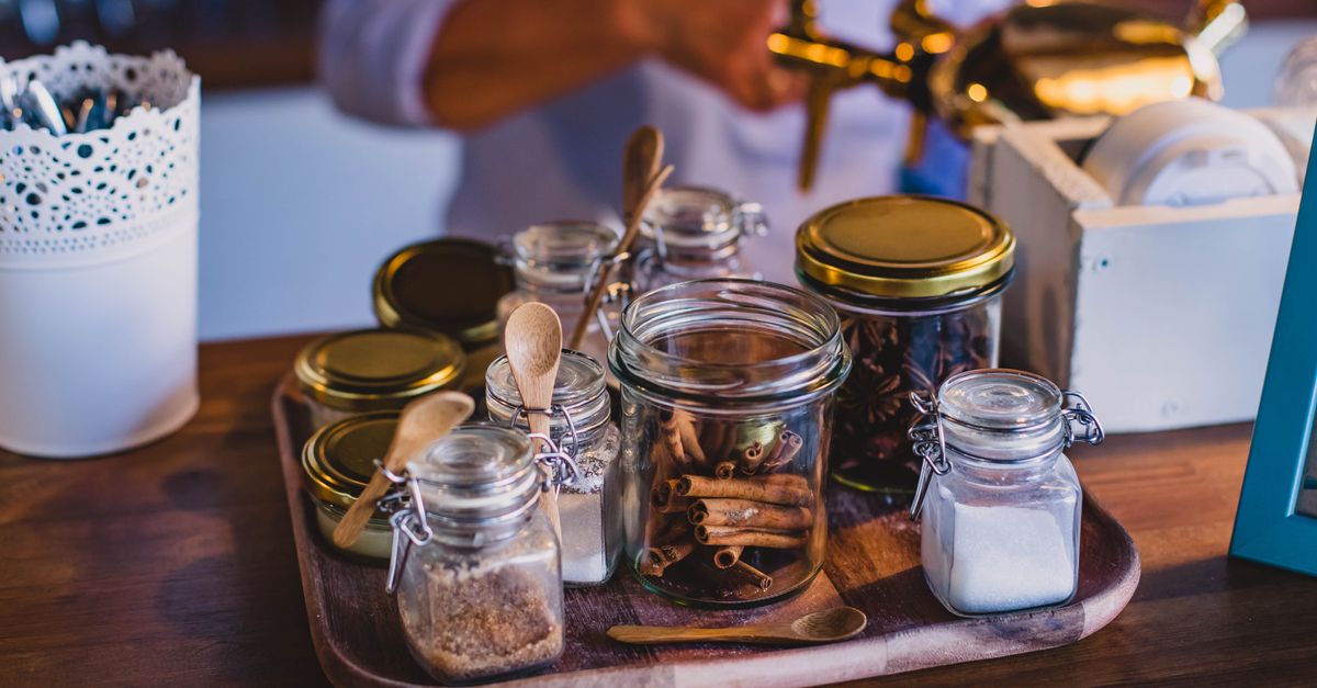 Plusieurs bocaux en verre remplis d'épices et de bâtons de cannelle disposés sur une planche en bois.
