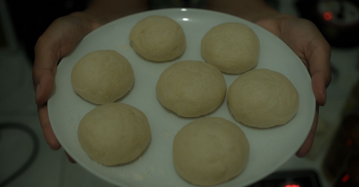 Des boules de pâte crue disposées sur une assiette blanche tenue à deux mains.